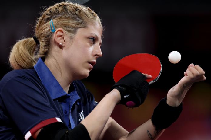 A female Para table tennis is serving the ball during a game.
