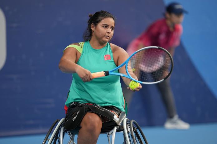 A female wheelchair tennis player prepares to serve