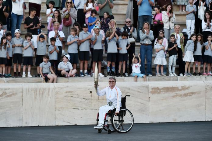 Beatrice Hess poses for a photo. She is holding the Paris 2024 torch in front of a crowd