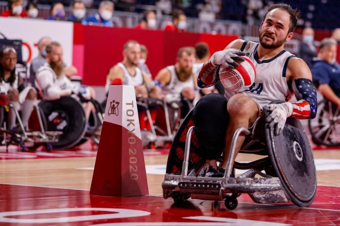 A male wheelchair rugby player carries the ball while crossing the try line