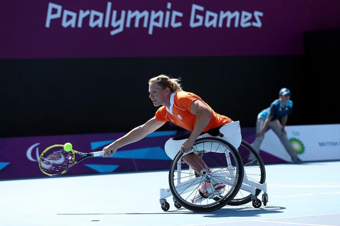 A female wheelchair tennis athlete reaches out to return a shot during a match.