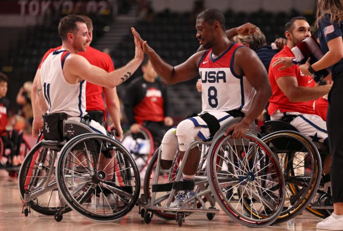 Two male wheelchair basketball players do a high-five to celebrate a victory