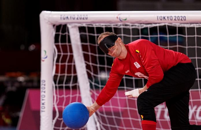 A male goalball player rolls the blue goalball in front of his net.