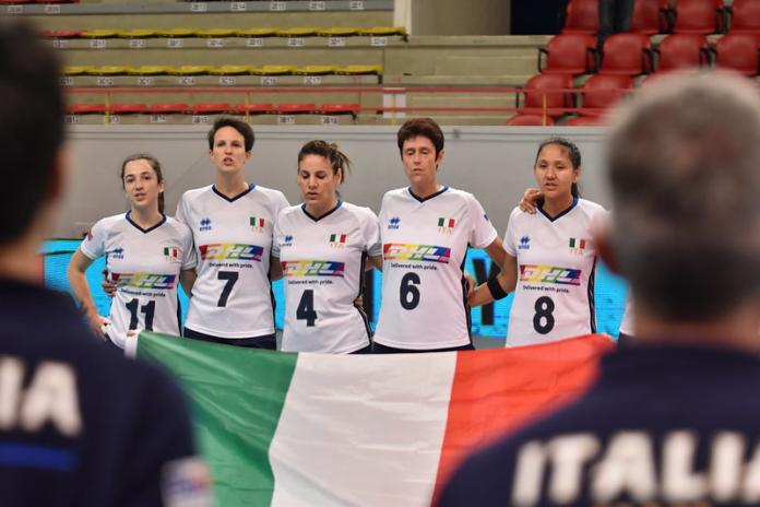 Five female sitting volleyball players stand in a line, holding the Italian flag