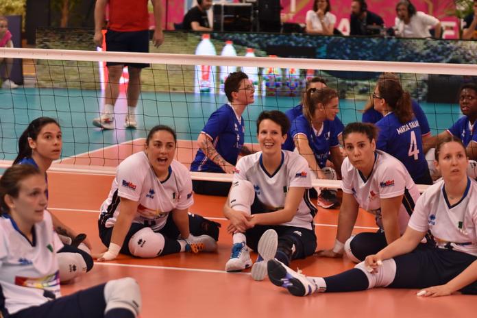 Six female sitting volleyball players sitting on the court and smiling