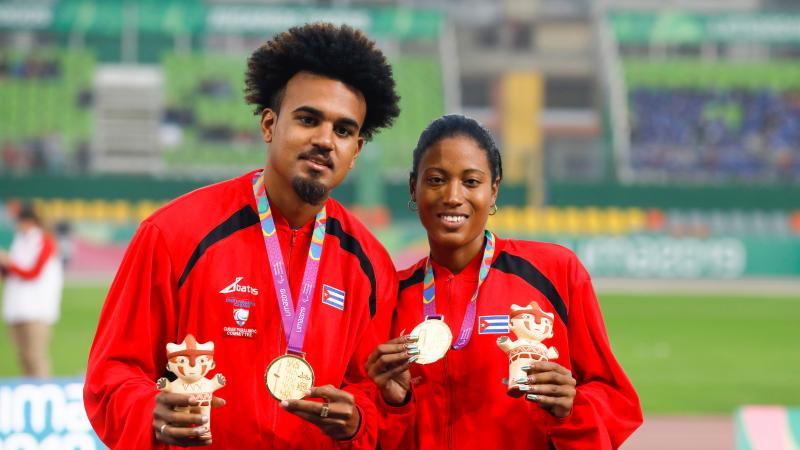 a female vision impaired runner and her guide hold up their gold medals