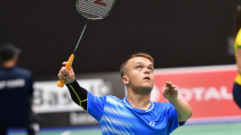 English short statured badminton player looks up about to hit the birdie