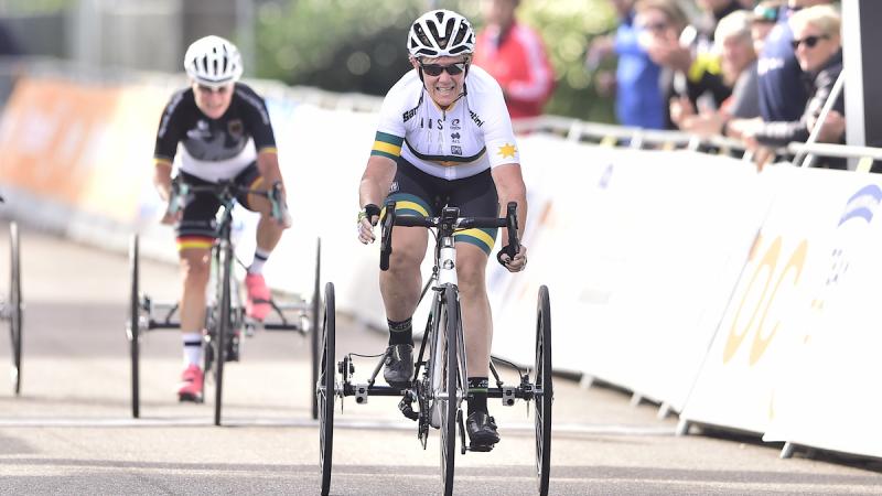 Australian woman in tricycle sprints toward finish line with opponent behind her