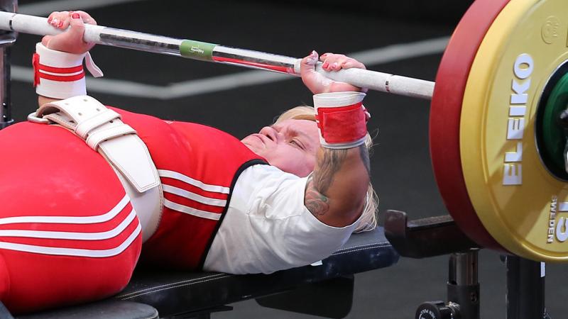 A female Para powerlifter with a red outfit preparing to lift the bar