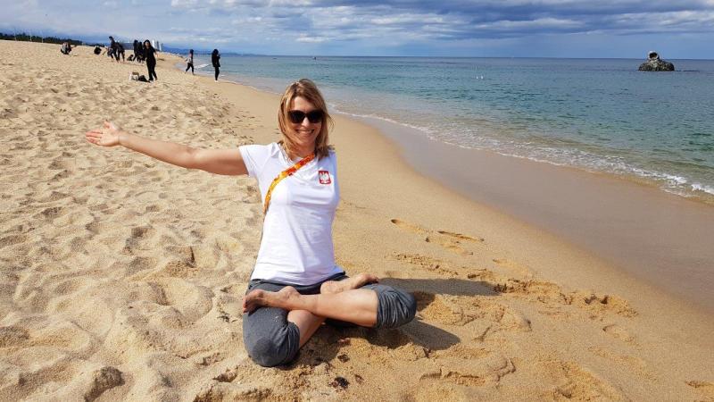 Woman with left arm amputation sits on sandy beach