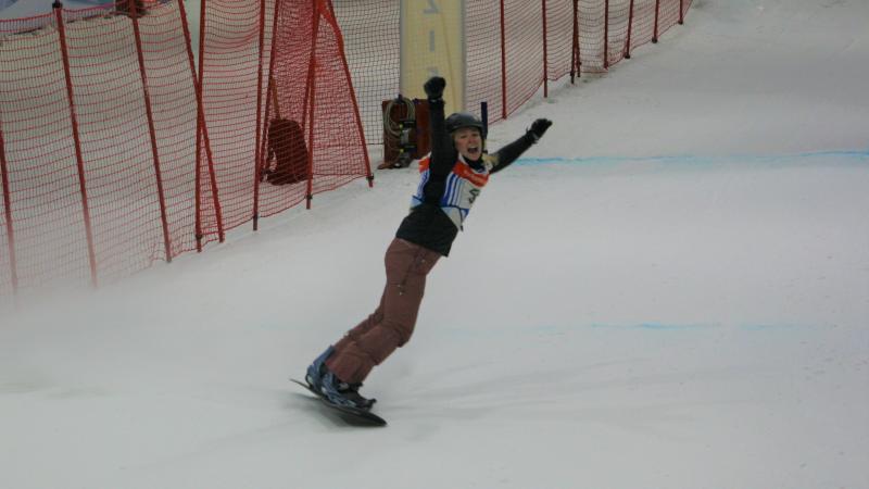 A female Para snowboarder stretching her arms in celebration in an indoor snow slope