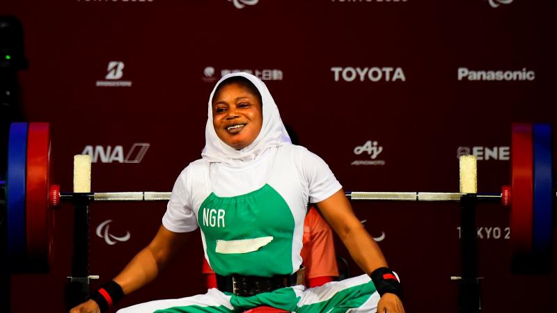 A woman sitting on the bench with her legs crossed and a smile on her face.