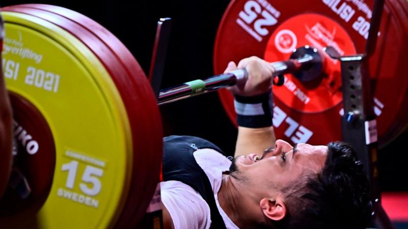 A young man lifting a bar in a Para powerlifting competition