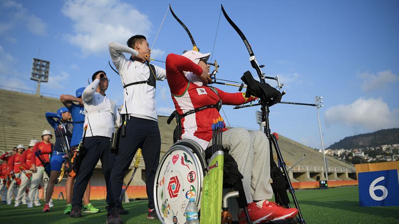 A female archer in a wheelchair shoots an arrow in a row of able-bodied archers.