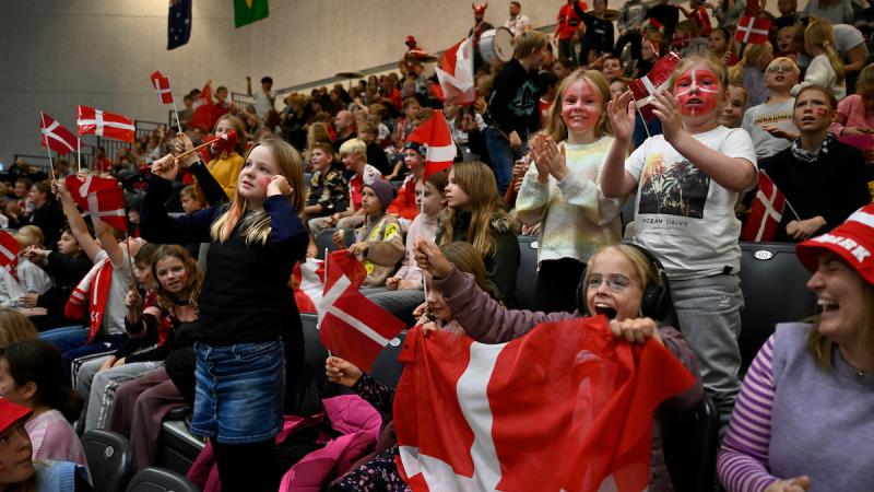 Children holding Denmark's flags fill the stands at a venue