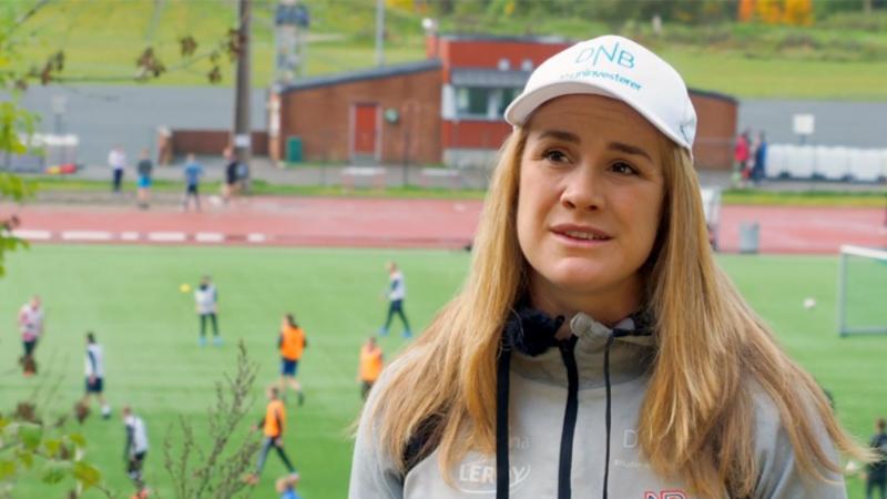 A woman with a white cap talking with a football match in the background