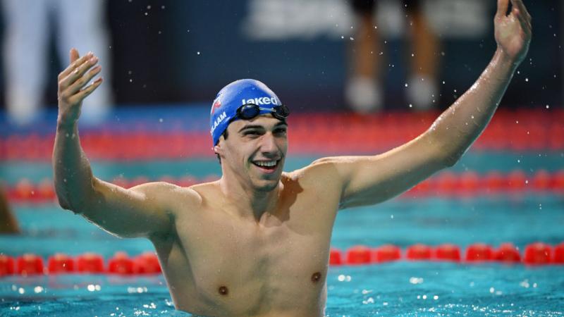 A male swimmer raises both hands in the pool to celebrate his victory.