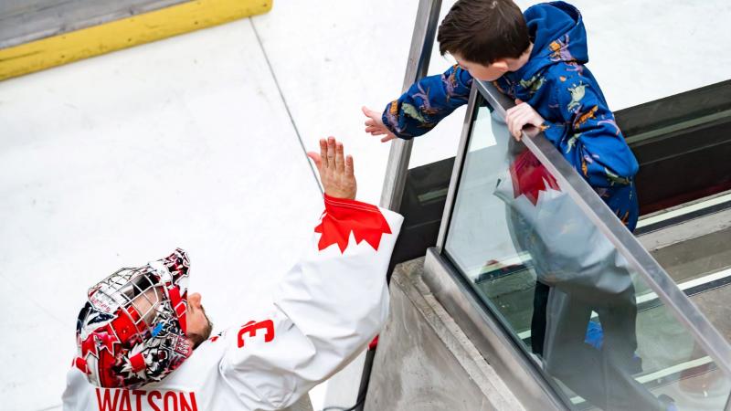 A hockey goaltender high-fiving a young fan in a rink