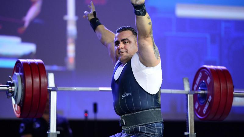 Para powerlifting athlete Hadi Darvishpoor sits in front of the weight and raises both arms.