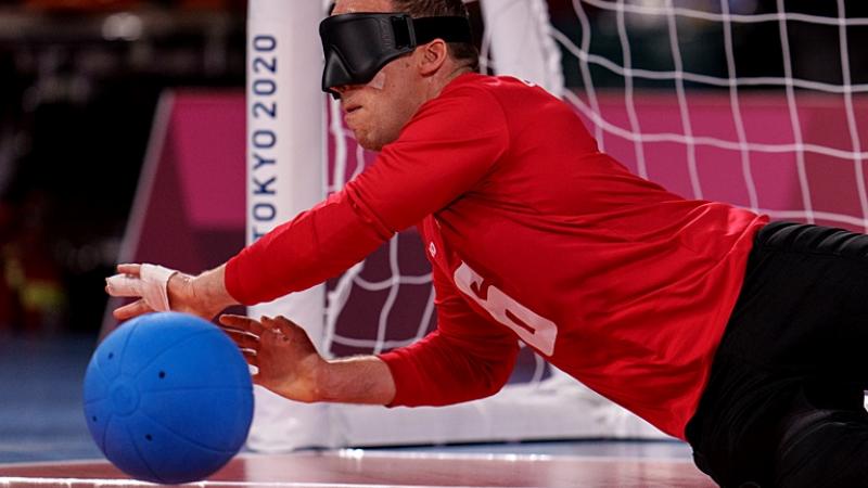 Two male goalball athletes are blocking the ball in front of a net