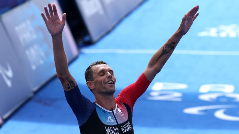 Para triathlete Alexis Hanquinquant raising his arms in celebration at the finish line
