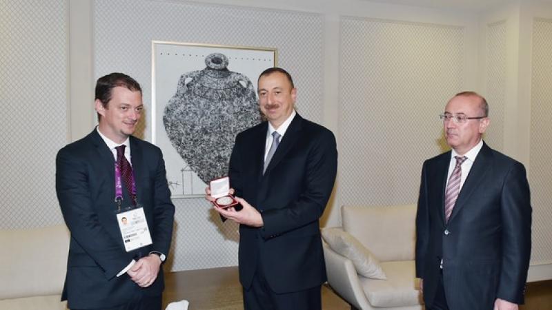 Three men in suits, one of them showing an award to the camera.