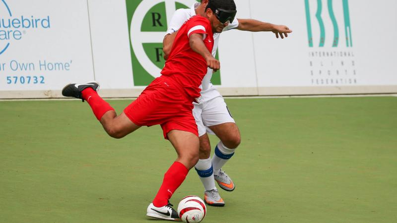 Two blindfolded football players fight for the ball