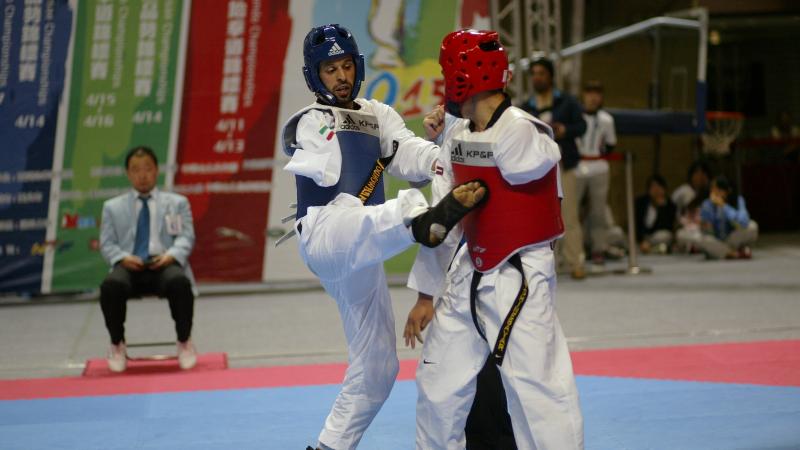 A para-taekwondo athlete does a jump kick to his opponent.