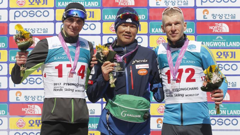 Three men on a podium, holding flower bouquets