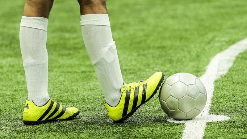 A man withbright yellow football boots rests his foot on a ball.