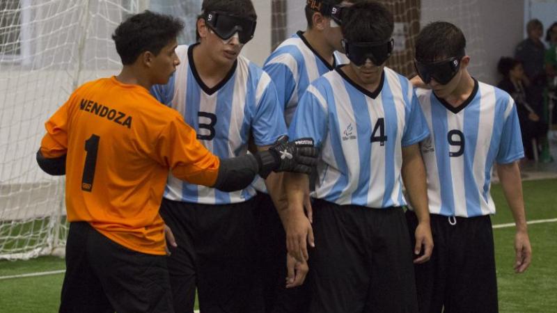 A blind football team organise themselves on the pitch