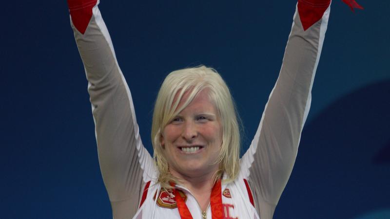 Swimmer raises her arms on the podium to celebrate her medal