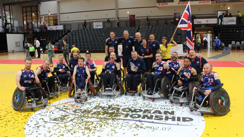 A group of men in wheelchairs surrounded by confetti and ribbons celebrate with the trophy