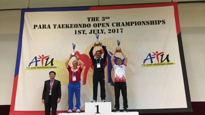 three men hold trophies on a podium