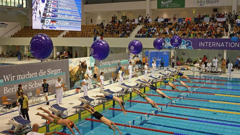 a group of male para swimmers dive into the pool