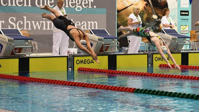 two female swimmers jump into the pool at the start of a race