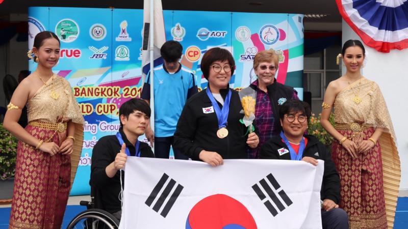 three South Korean shooters with their medals and their flag