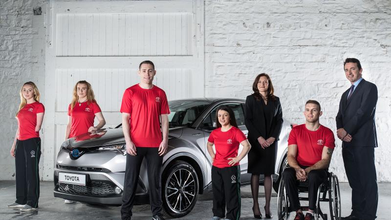 Seven people in front of a car. Six are standing and one is in a wheelchair
