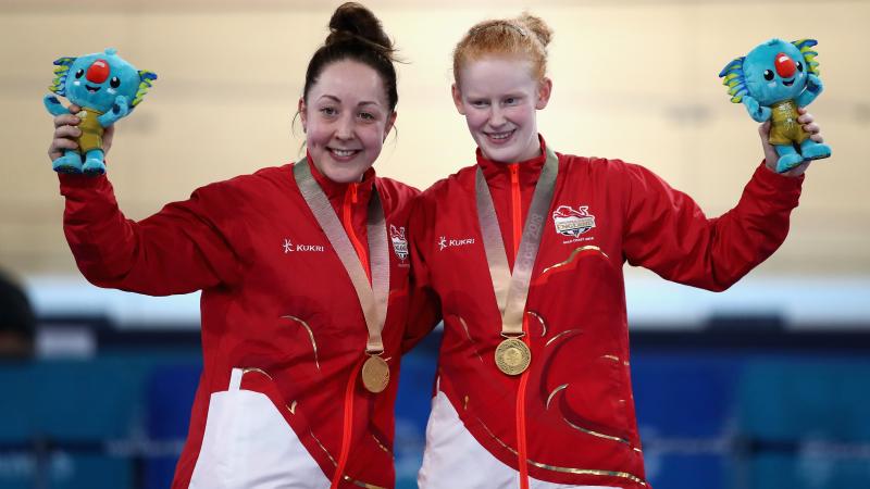 two female Para cyclists stand on the podium with their gold medals