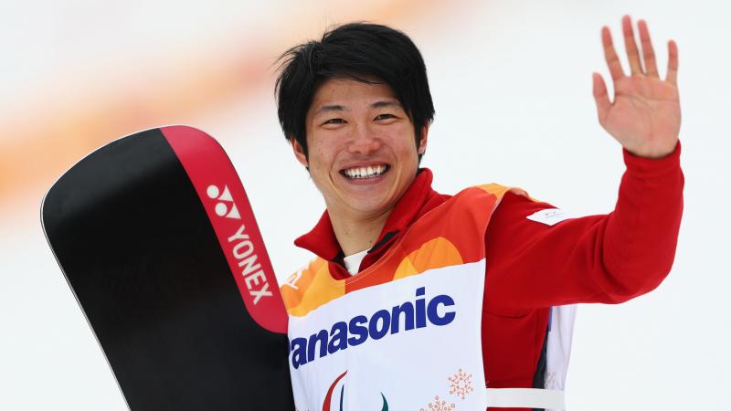 male Para snowboarder Gurimu Narita holds his snowboard and waves to fans