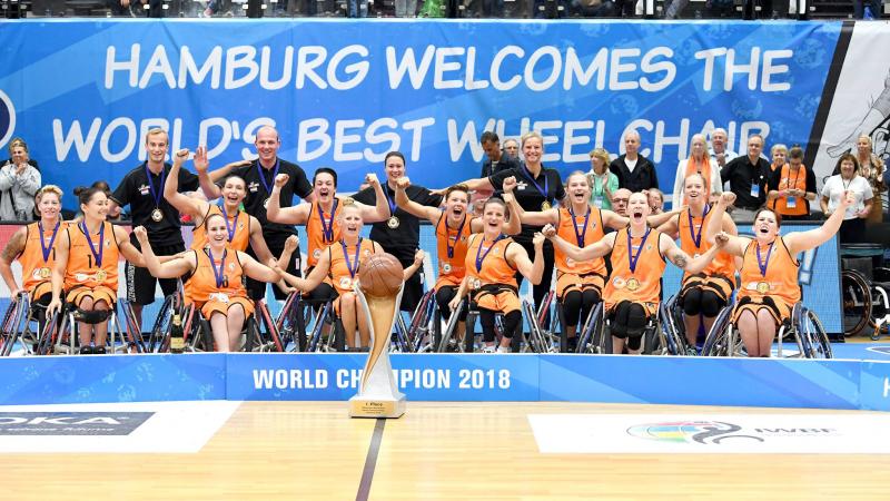 A group of women in organge vests celebrate with a large trophy after winning the world title