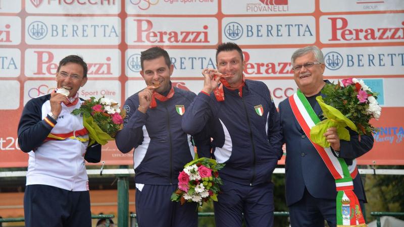 three male Para shooters with Francesco Nespeca in the middle, biting their medals