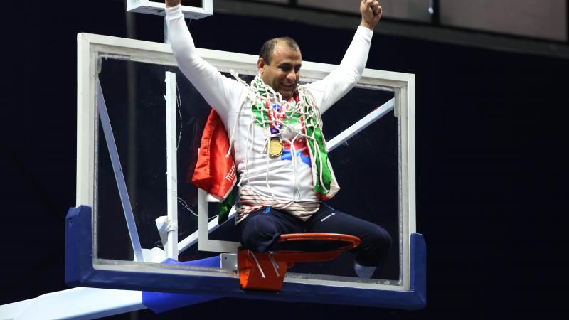 male wheelchair basketball player Morteza Ebrahimi sitting on top of the basketball hoop raising his arms