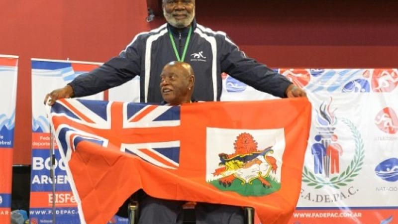 male boccia athlete Steve Wilson on the podium holding up a Bermuda flag