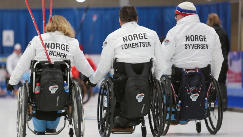 three wheelchair curlers with their backs to the camera with Norway on their jackets