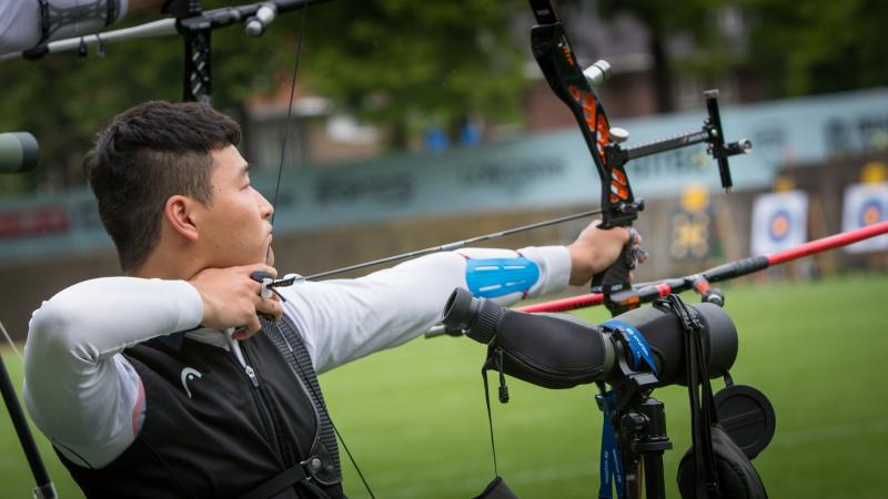 Korean male archer pulls back on his bow string aiming for a target