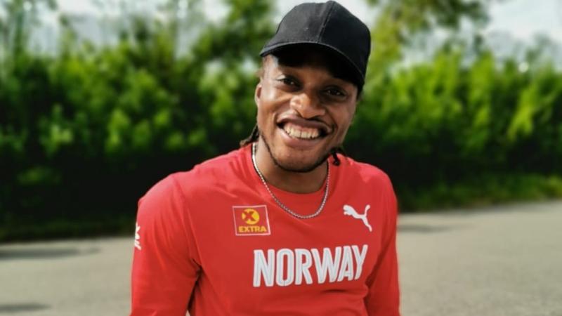 A man with a shirt a long-sleeved red shirt written Norway seated on the sidewalk