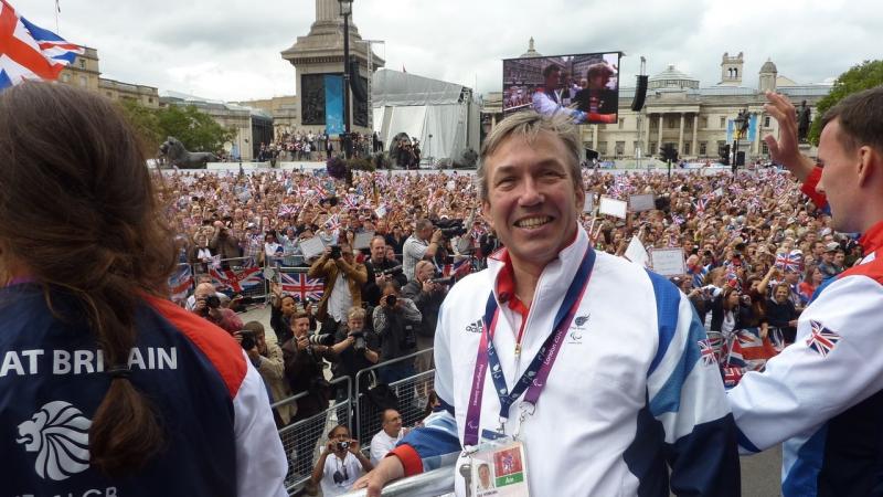 British man in wheelchair smiling in front of a big crowd of people