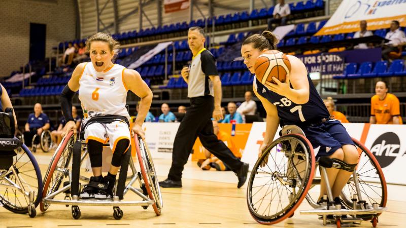 British female wheelchair basketball player makes a move with the ball while a Dutch player turns to defend her