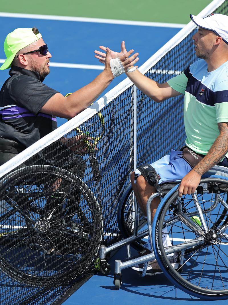 two male wheelchair tennis players shake hands at the net